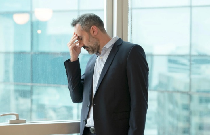 uomo preoccupato con una mano sulla fronte accanto alla finestra
