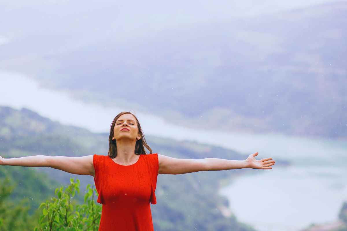 Donna a braccia aperte e con volto rivolto verso il cielo accoglie le prime gocce di pioggia