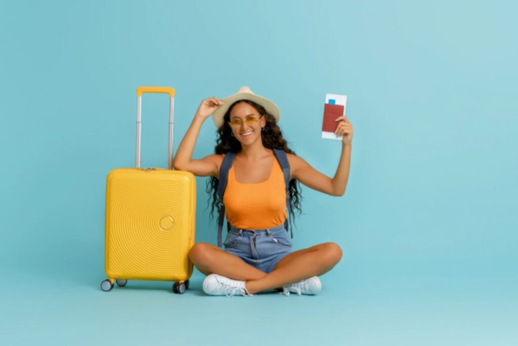 ragazza seduta per terra con uno zaino in spalla e accanto un trolley