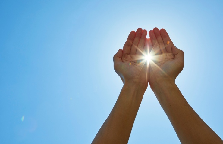 Due mani che nascondono giocosamente il Sole in una giornata serena