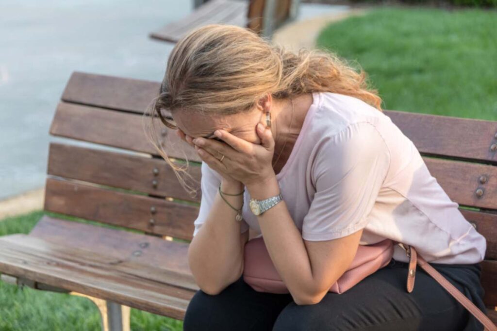 donna disperata seduta su una panchina con le mani in faccia
