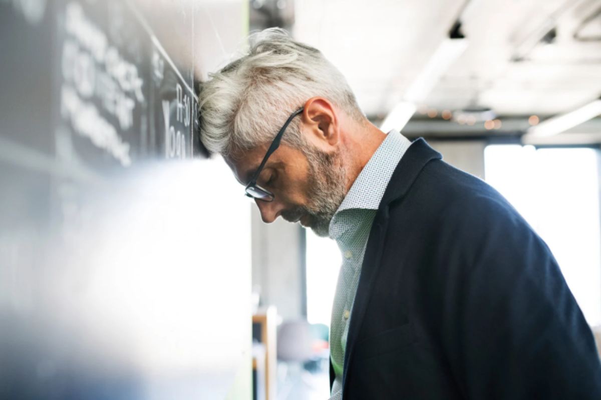 uomo disperato con la fronte appoggiata al muro