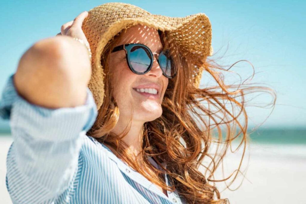 donna sorridente in spiaggia con occhiali a cappello di paglia