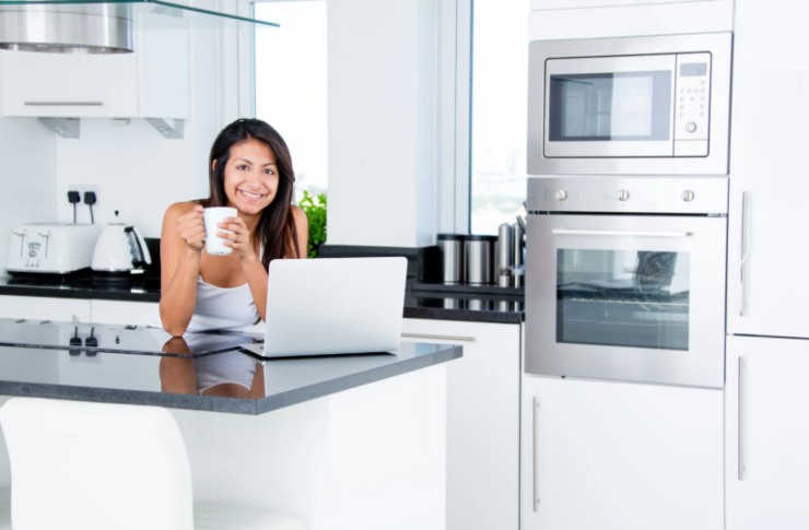 donna che sorride in cucina con una tazza in mano davanti al computer