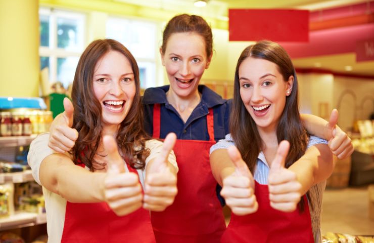 tre commesse del supermercato che sorridono con i pollici in su