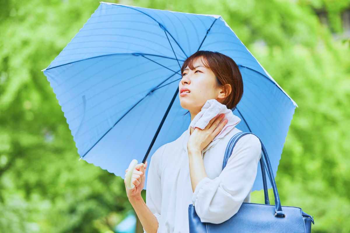 Donna con ombrello in mano che asciuga il sudore con una tovaglia