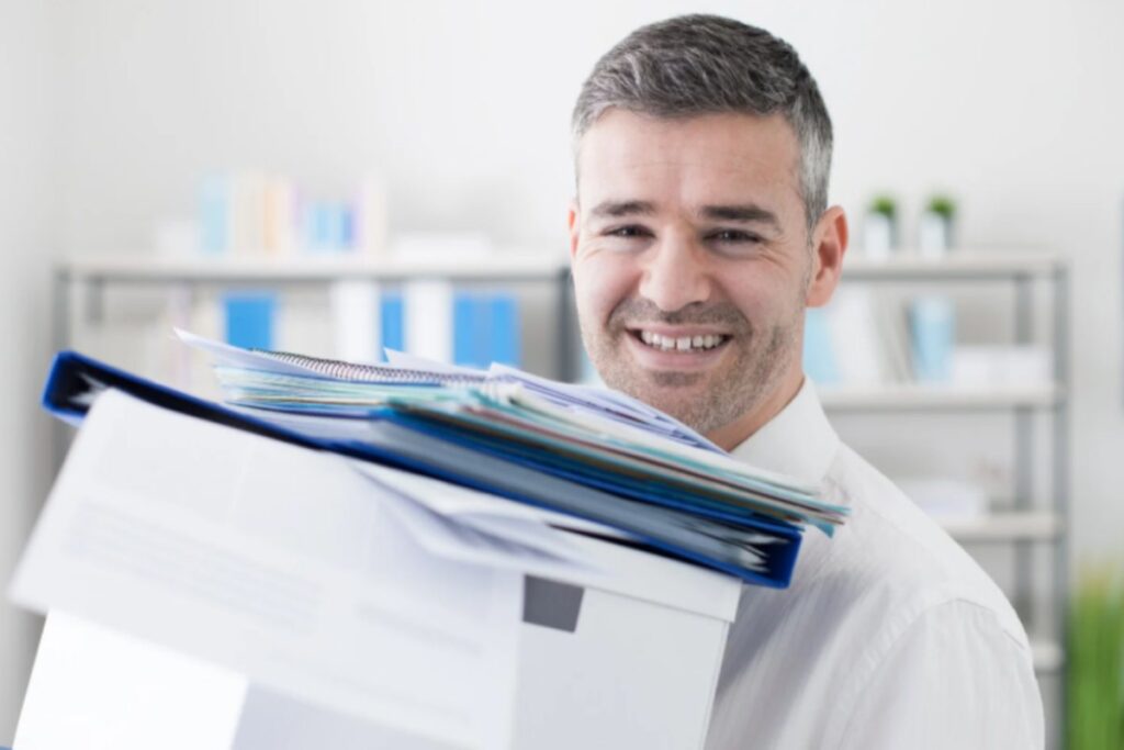 uomo che sorride con in mano degli scatoloni e dei faldoni