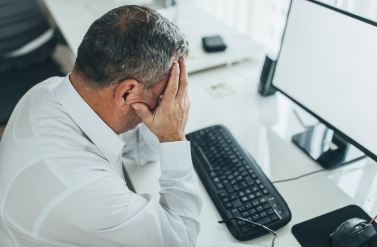 uomo con le mani in faccia seduto davanti al computer
