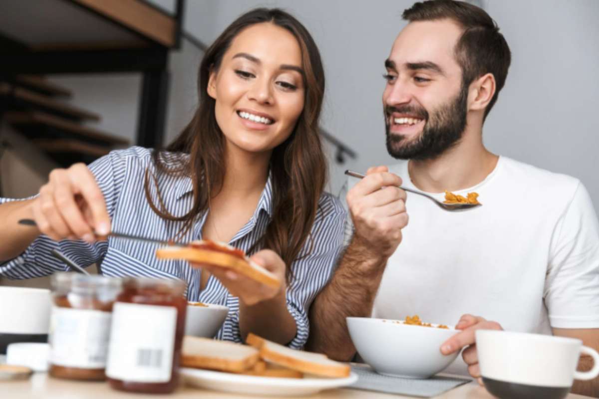 uomo e donna seduti al tavolo che fanno colazione e sorridono