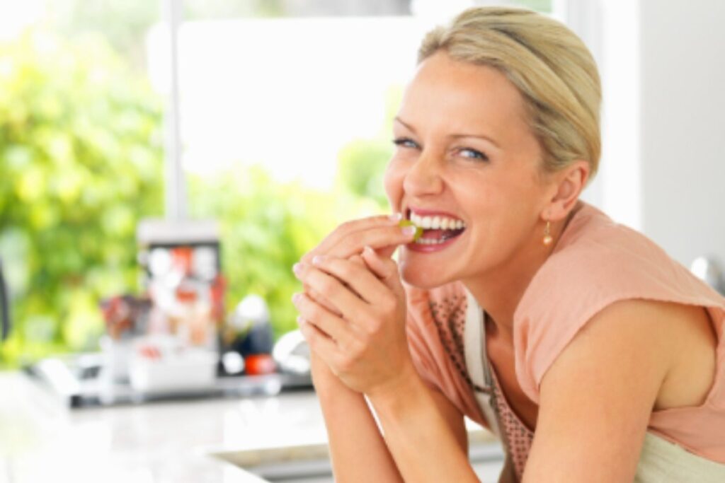 donna in cucina che sorride e mangia un chicco di uva