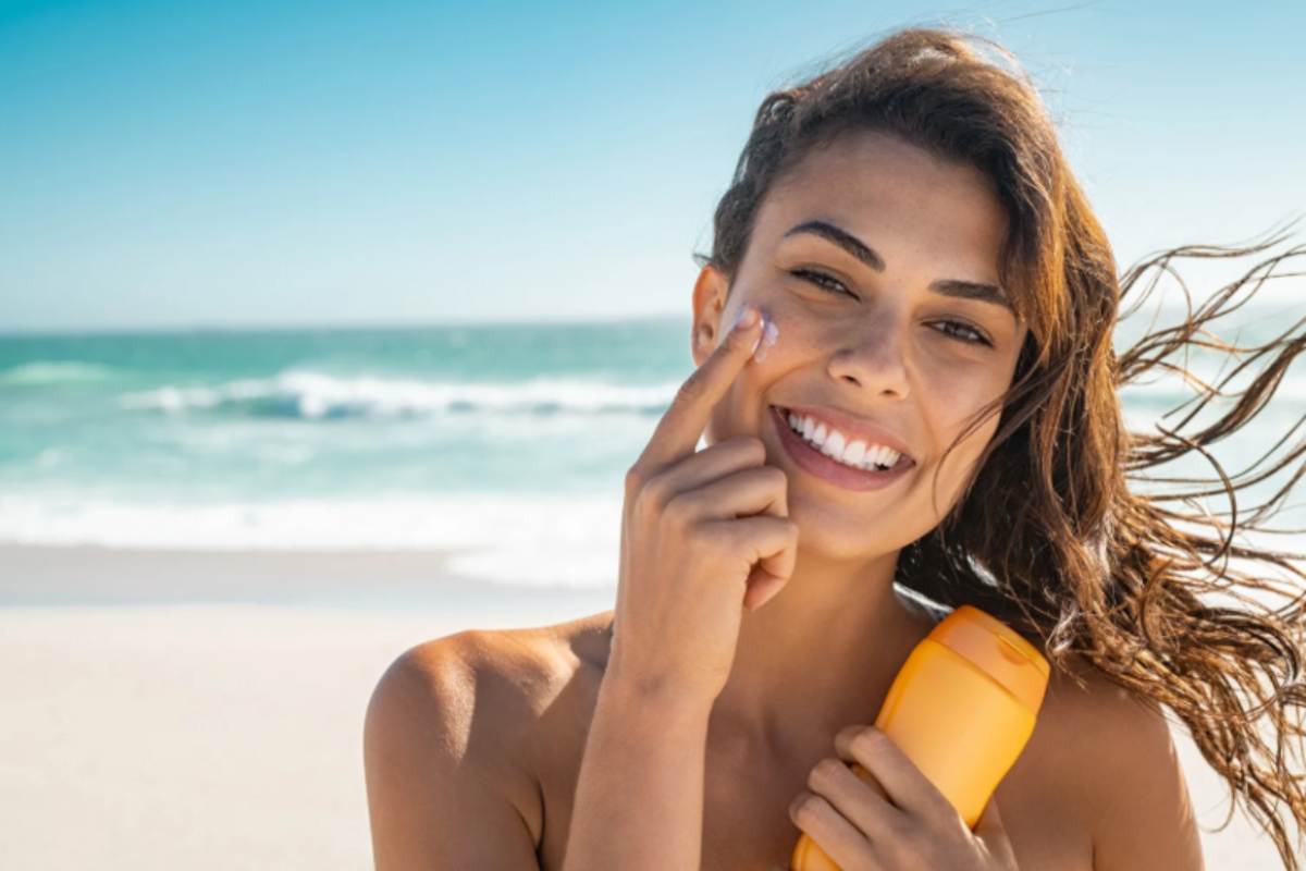 donna in spiaggia che si mette la crema solare sul viso