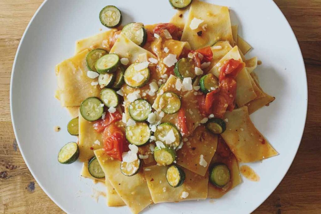piatto fumante di maltagliati con zucchine, pomodorini e formaggio grattugiato