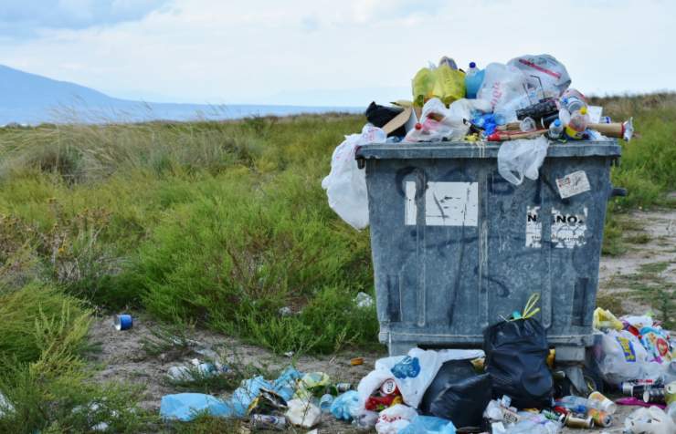 bidone pieno di rifiuti in mezzo ad un prato