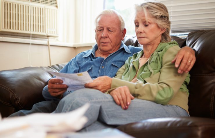 coppia di anziani tristi seduti sul divano che leggono un foglio