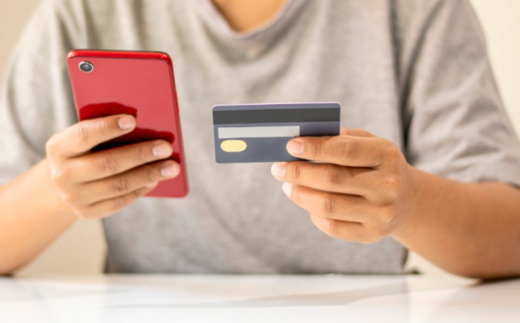 uomo con in mano il cellulare e nell'altra mano un bancomat