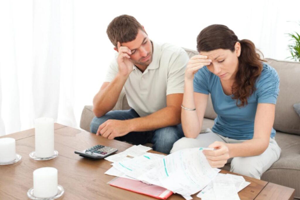 uomo e donna seduti sul divano preoccupati con davanti dei fogli e una calcolatrice