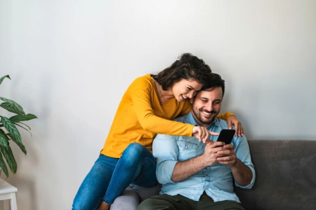 uomo e donna che sorridono mentre guardano qualcosa sul cellulare