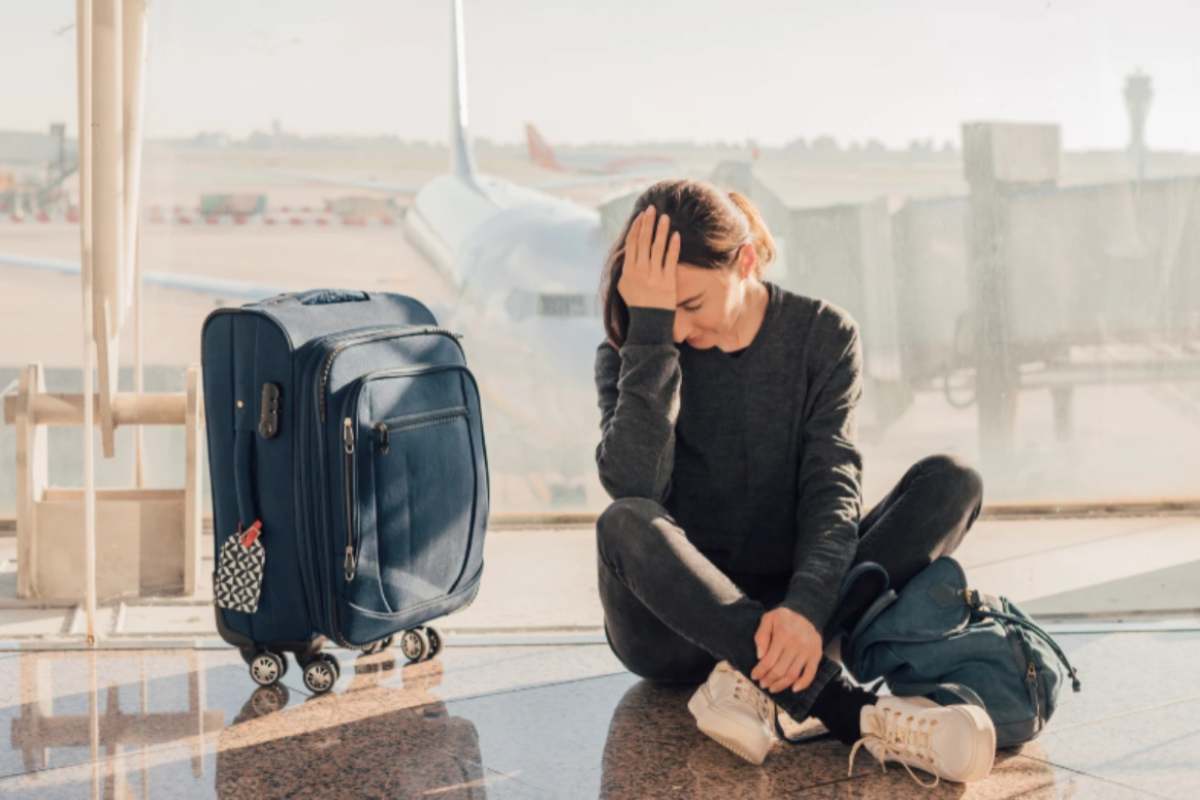 donna disperata seduta sul pavimento in aeroporto con accanto una valigia
