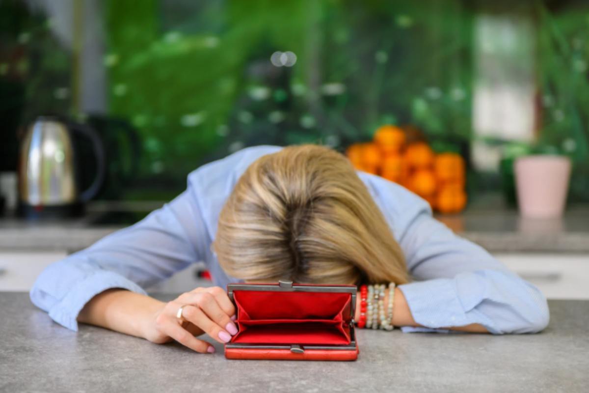 donna con la testa sul tavolo e davanti a lei un portafoglio vuoto