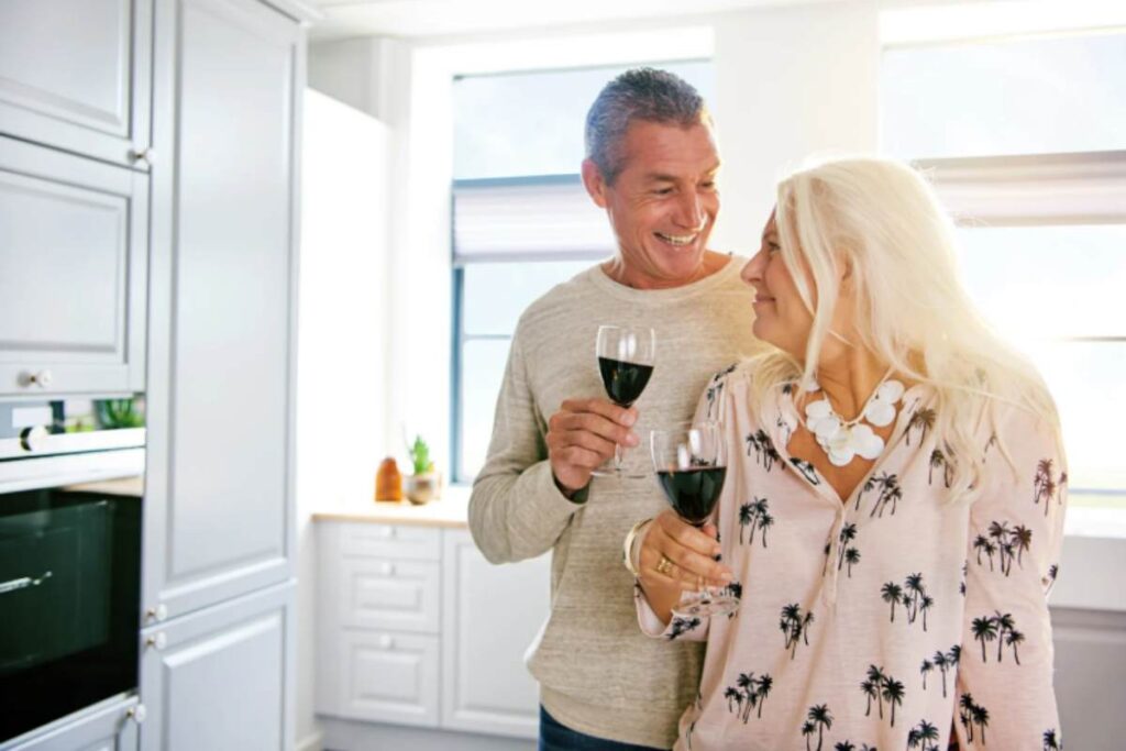 uomo e donna in cucina sorridenti con in mano due calici di vino rosso