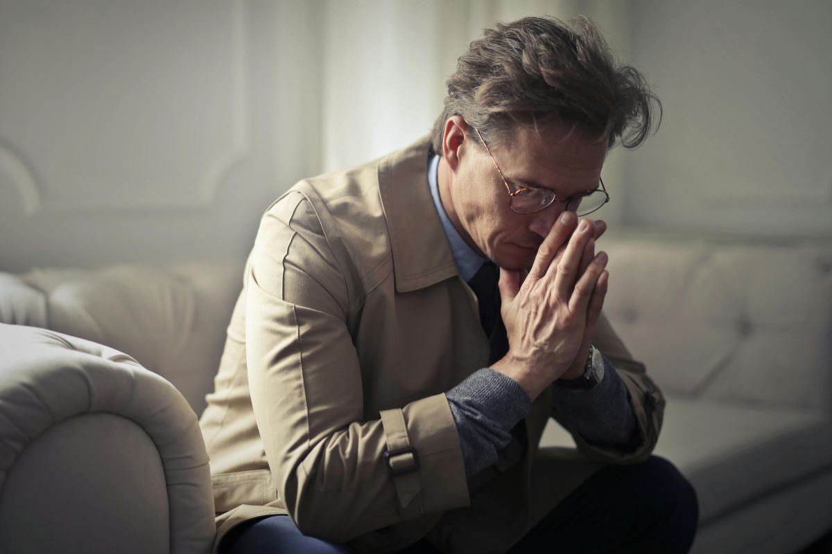 uomo seduto sul divano con le mani congiunte davanti al viso