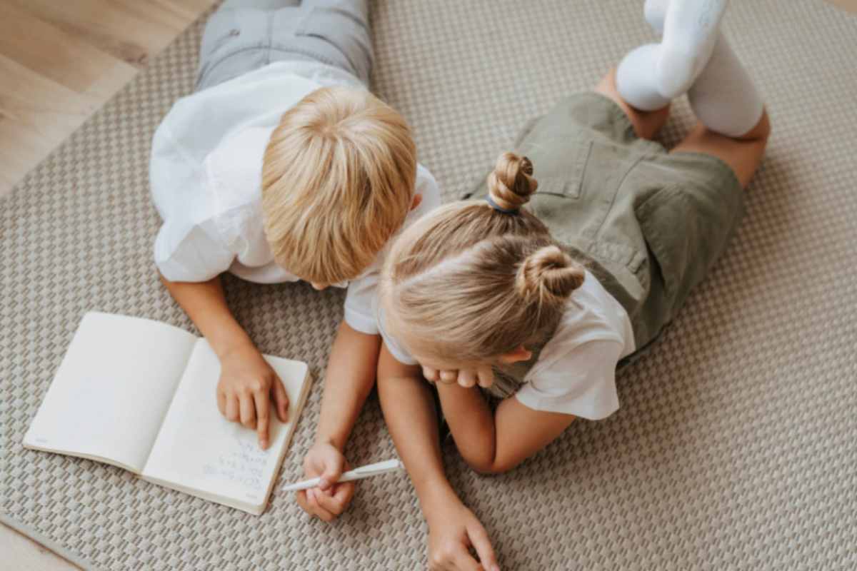 due bambini stesi a terra che fanno i compiti