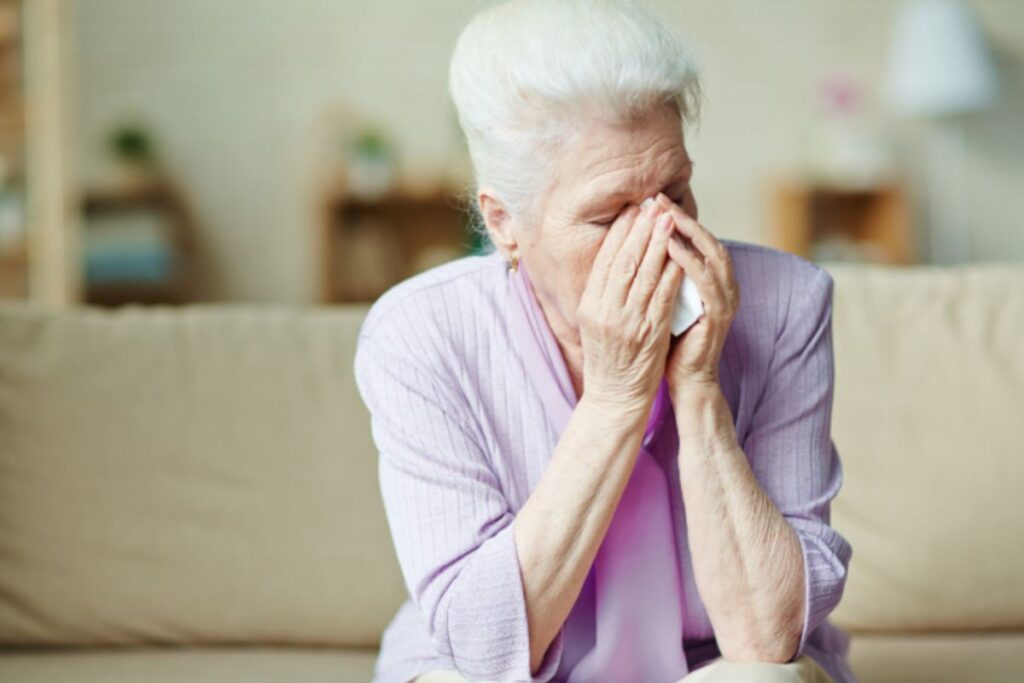 donna anziana seduta sul divano disperata con le mani in faccia