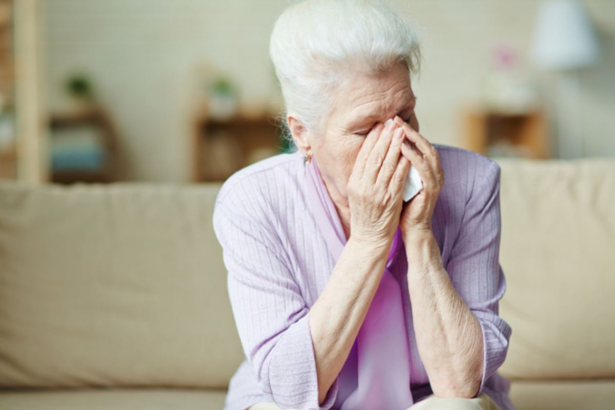 donna anziana seduta sul divano disperata con le mani in faccia