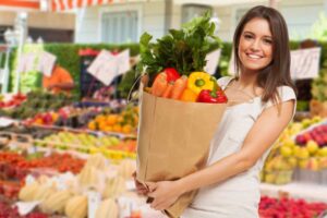donna che sorride al supermercato mentre tiene una busta piena di ortaggi