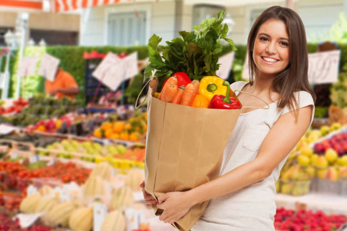 donna che sorride al supermercato mentre tiene una busta piena di ortaggi