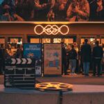 ciak e pellicola in primo piano e gente che si appresta ad entrare al cinema in secondo piano