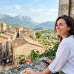 Panorama borgo medievale Abruzzo con turista, calice di vino e montagne del Gran Sasso sullo sfondo durante una vacanza estiva.