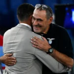 Raffaele Palladino ritratto di spalle abbraccia un sorridente Maurizio Sarri con t-shirt di rappresentanza della Lazio.
