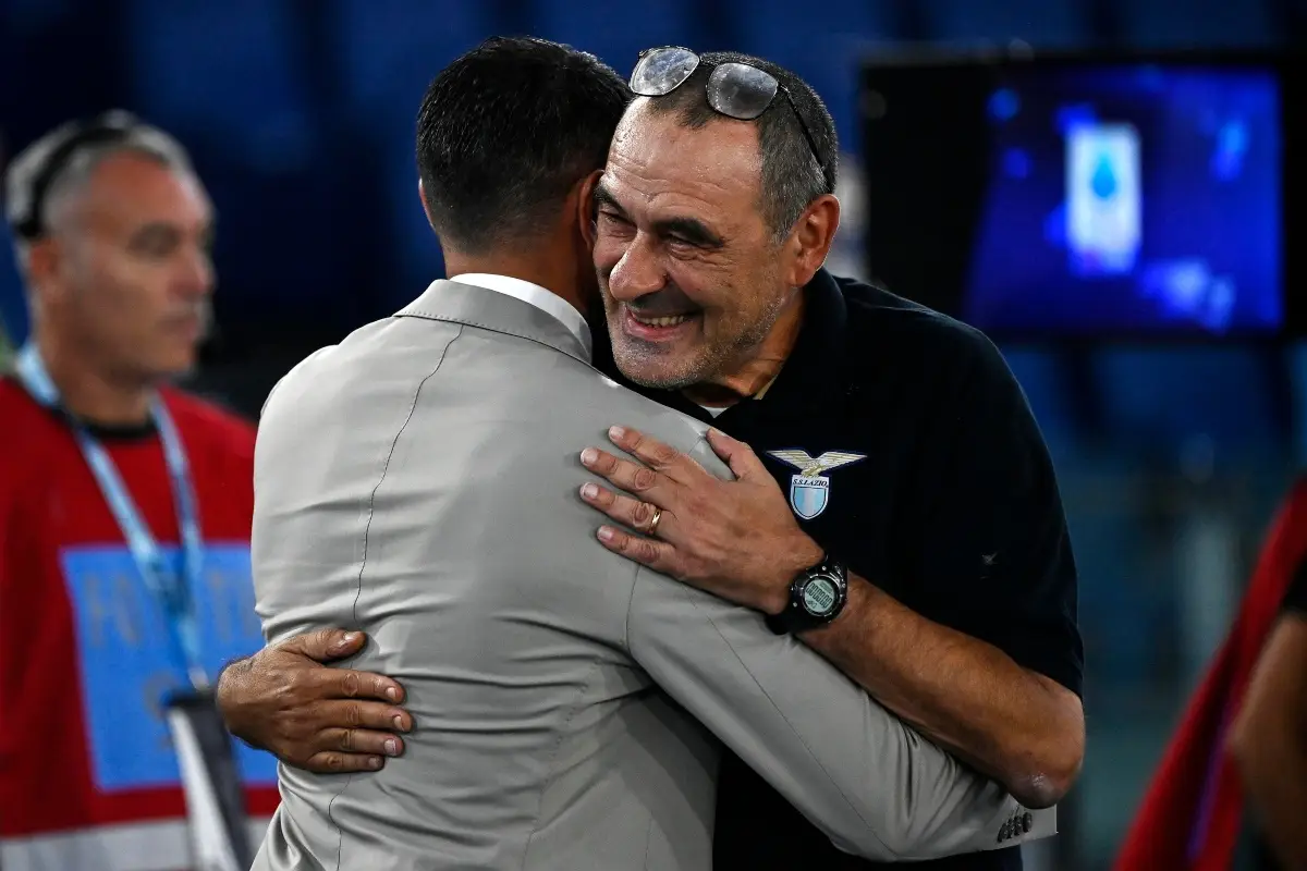 Raffaele Palladino ritratto di spalle abbraccia un sorridente Maurizio Sarri con t-shirt di rappresentanza della Lazio.