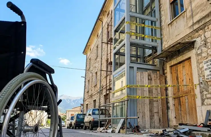 Cantiere bloccato dell'ascensore esterno Inail a Sulmona con sedia a rotelle in primo piano e nastri di pericolo.