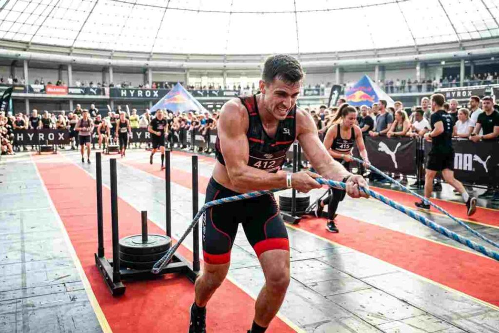 Atleta durante una gara di Hyrox mentre esegue il pull della slitta con corda in un evento di fitness ibrido indoor.