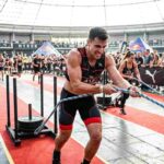 Atleta durante una gara di Hyrox mentre esegue il pull della slitta con corda in un evento di fitness ibrido indoor.
