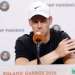 Jannik Sinner con una espressione stanca si tiene il volto con le mani davanti ad un microfono in conferenza stampa.