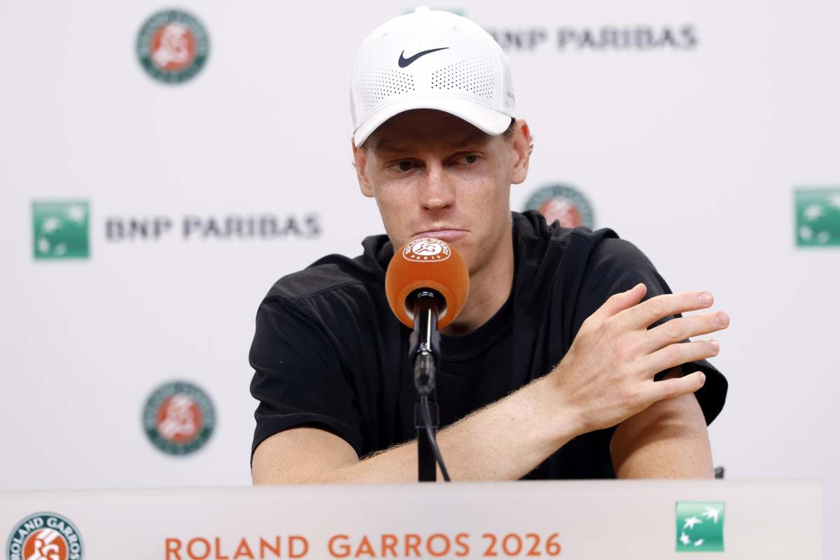Jannik Sinner con una espressione stanca si tiene il volto con le mani davanti ad un microfono in conferenza stampa.