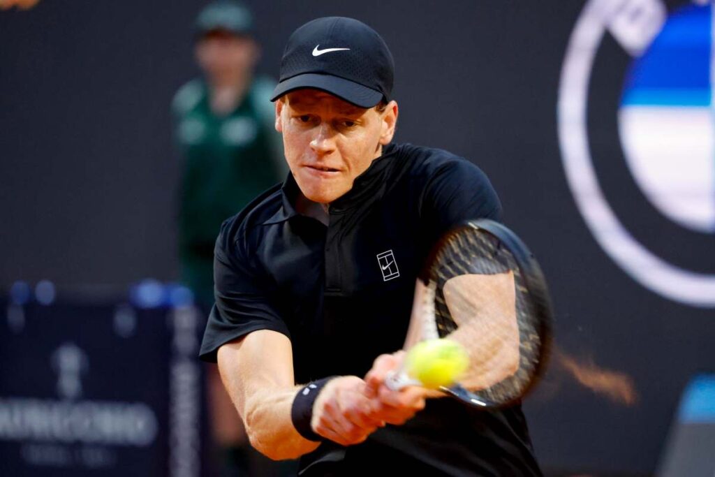 Jannik Sinner colpisce di rovescio in doppie mani la palla di tennis con la racchetta.