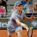 Jannik Sinner colpisce la palla in dritto di destro mentre indossa un completo grigio su terra rossa.