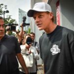 Jannik Sinner con t-shirt nera e berretto bianco al cospetto di giornalisti e fotografi in esterna.