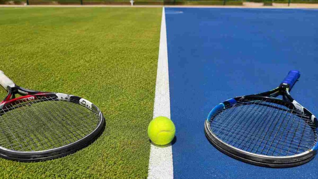 Campo da tennis diviso tra erba e cemento con pallina e racchette, simbolo del passaggio di superficie nel tennis professionistico.