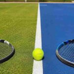 Campo da tennis diviso tra erba e cemento con pallina e racchette, simbolo del passaggio di superficie nel tennis professionistico.