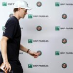 Jannik Sinner inquadrato di profilo davanti al cartonato degli sponsor.